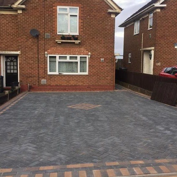 Paved driveway in front of a red brick house with neighbouring properties visible.