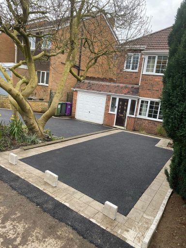 A newly paved driveway with stone borders next to a brick house and trees.