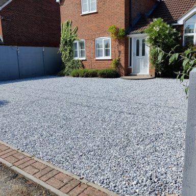 Gravel driveway in front of a brick house with a white door and green plants.