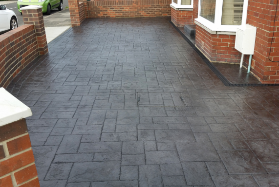 Patterned dark grey paving stones in a driveway, bordered by brick walls.