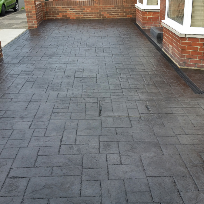 Patterned dark concrete driveway beside a brick house.