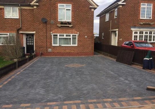 Newly laid grey driveway with brick edges between two brick houses.